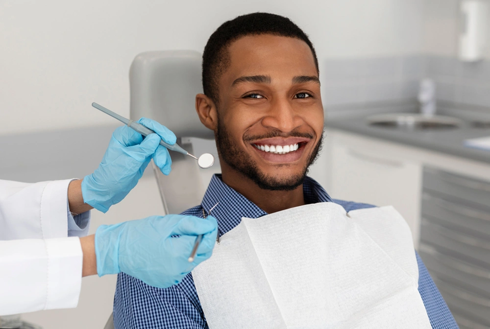 Cropped of dentist tools in doctor hands and cheerful african guy in dentist chair