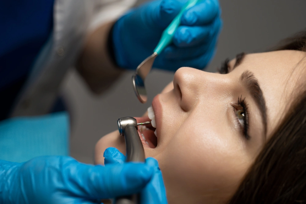 dentist in blue gloves filling the beautiful smiling woman patient's root canal using mirror and drill in clinic